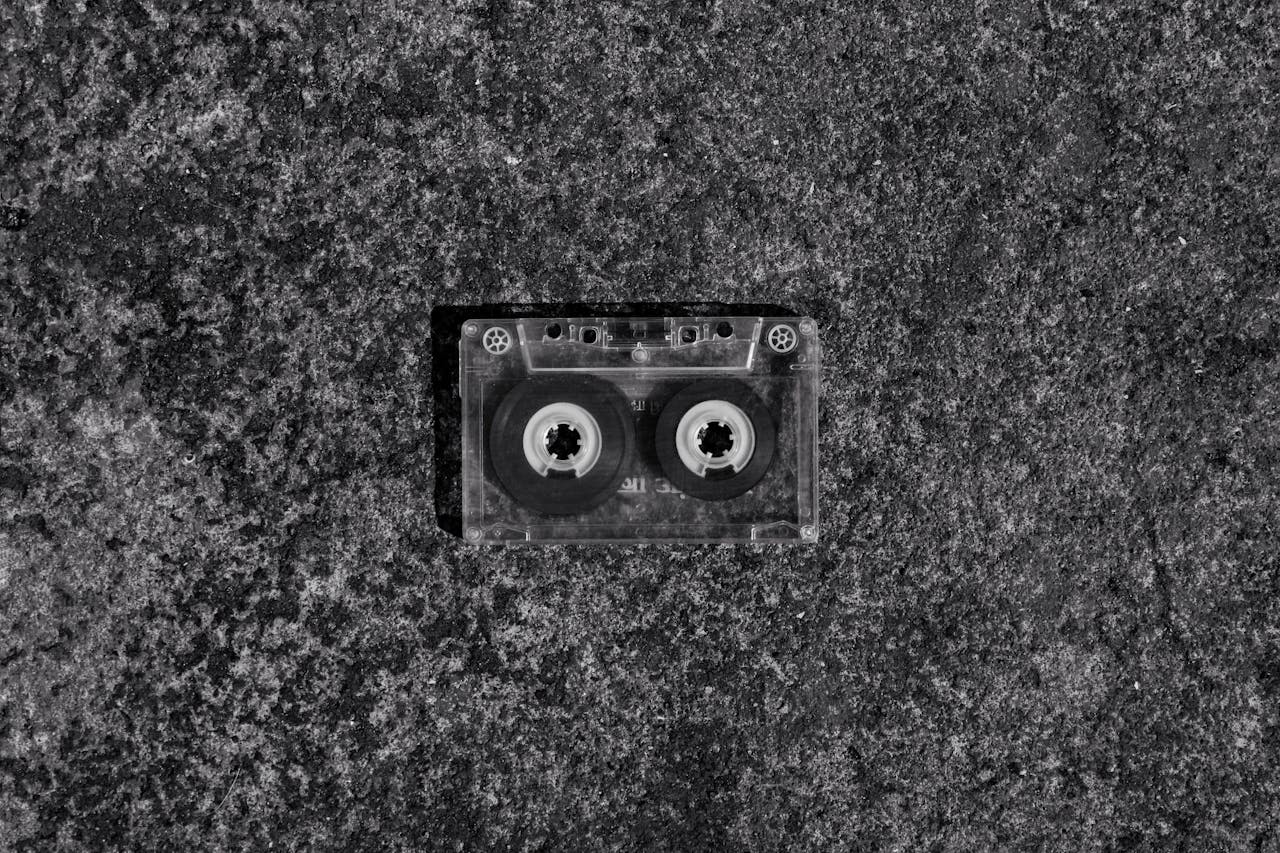A black and white photo of a vintage cassette tape lying on a textured concrete background.